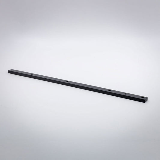 A long, thin black brass metal bar with pre-drilled holes, photographed diagonally on a light gray gradient background.