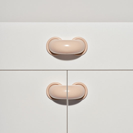 White cabinet with pale blush colored macaroni-shaped handles on a white background