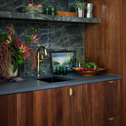 A marble bar with integrated sink and brass faucet with fluted wood cabinetry and brass tab pulls