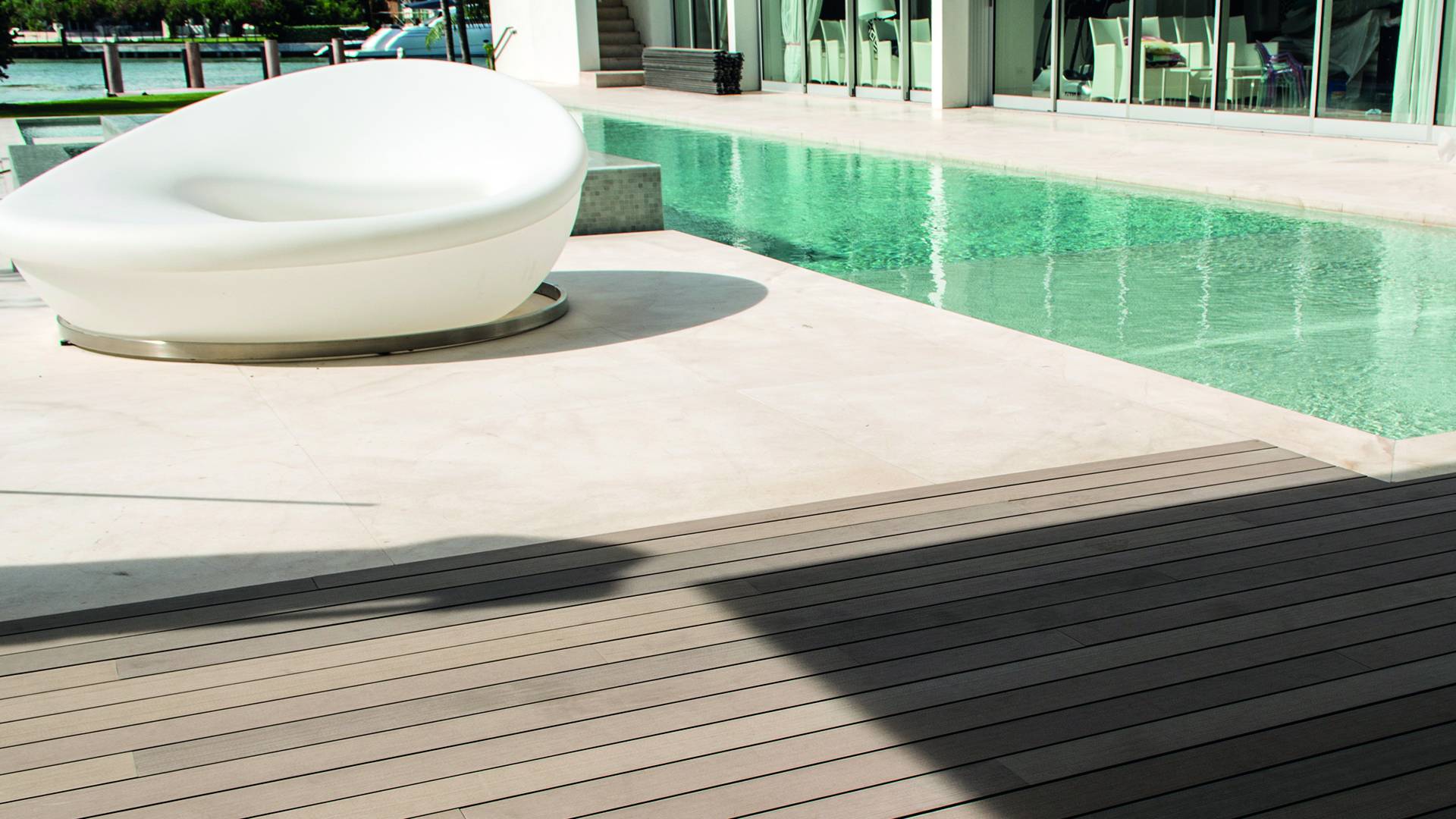 A large white nest shaped outdoor lounge chair sitting on Esthec decking at poolside.