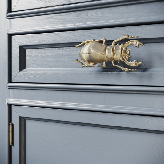 a  naturalistic stag beetle cabinet pull in a shiny brass finish installed on blue gray cabinet drawers