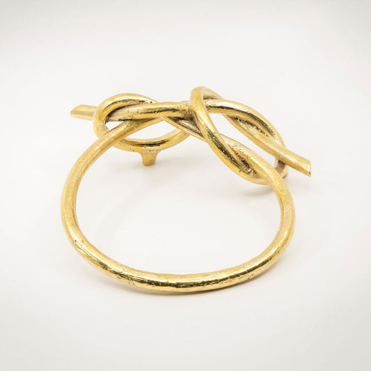A large twisted gold-toned metal sculptural cabinet pull with a natural brass finish, photographed on a light gray background.