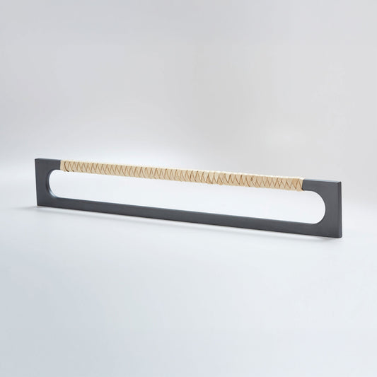 A modern long rectangular cabinet pull handle with a dark oil-rubbed bronze metal frame with an oval shaped-cutout and a light tan leather woven grip, shown on a white background.