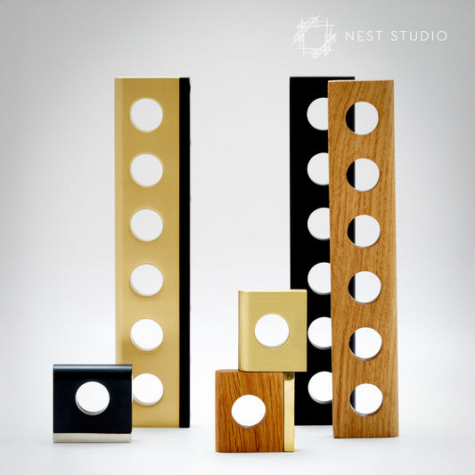 A set of modern decorative architectural cabinet pulls by Nest Studio, featuring rectangular panels with circular cutouts in black, gold, and natural wood finishes, arranged on a light gray background.