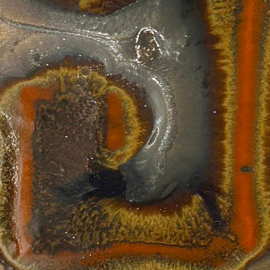 Close-up of a glossy ceramic tile or coaster featuring a marbled pattern of orange, brown, gray, and black with a textured, metallic-like finish.