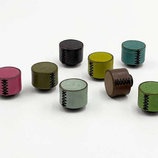 A set of small leather cabinet knobs in various colors including pink, olive green, black, yellow, teal, brown, and light green, each featuring a black zigzag stitched pattern on the side, arranged on a plain white background.