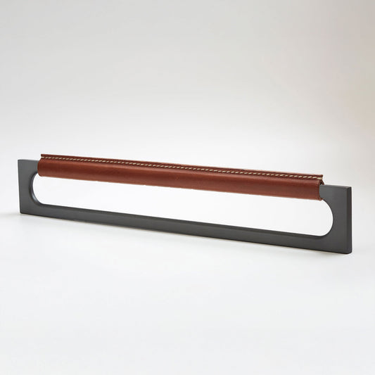 A modern rectangular metal cabinet pull with a central cutout, featuring a light brown leather strap stitched across the top, shown on a clean grey studio background.