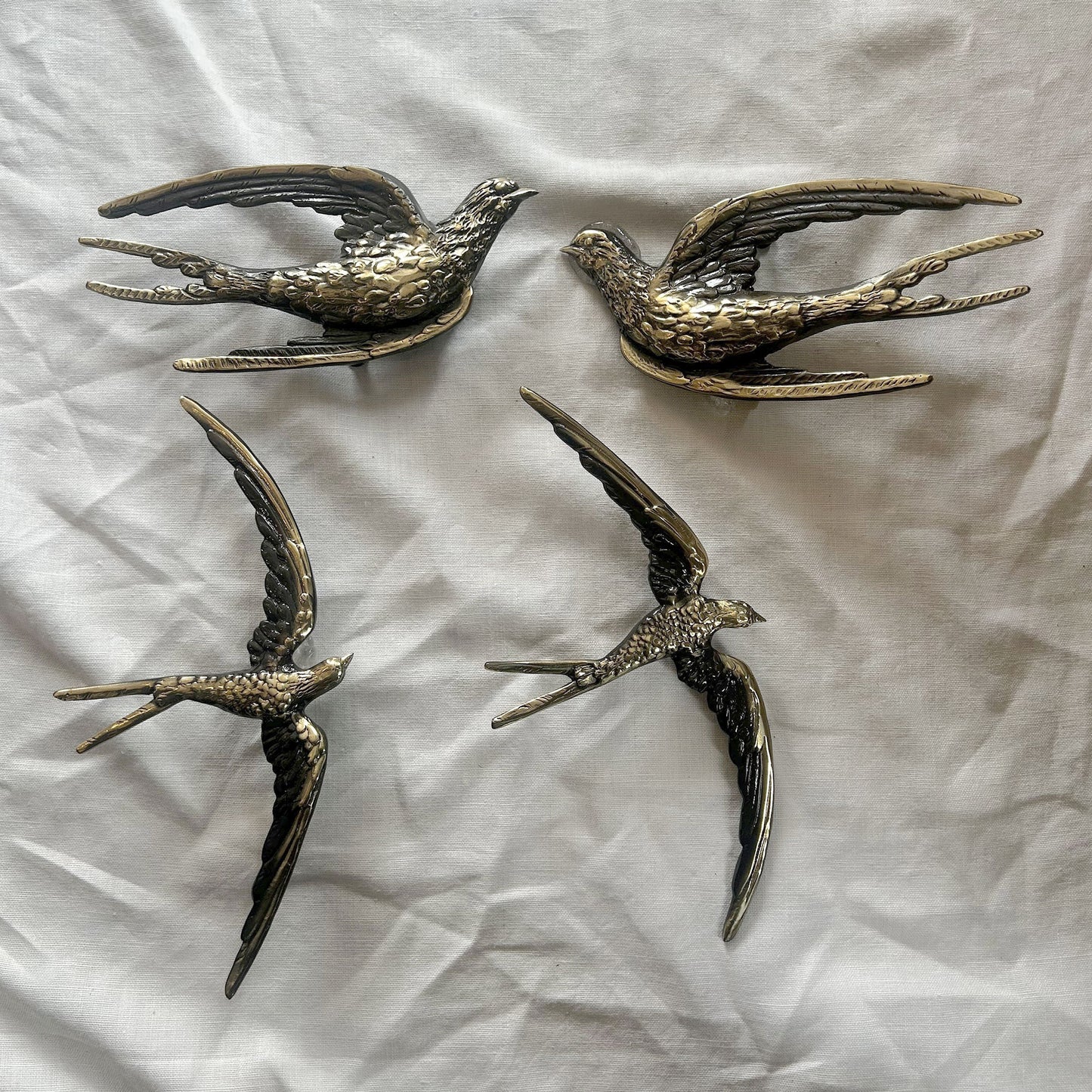 Four antique brass realistic bird shape cabinet pulls on a textured white surface