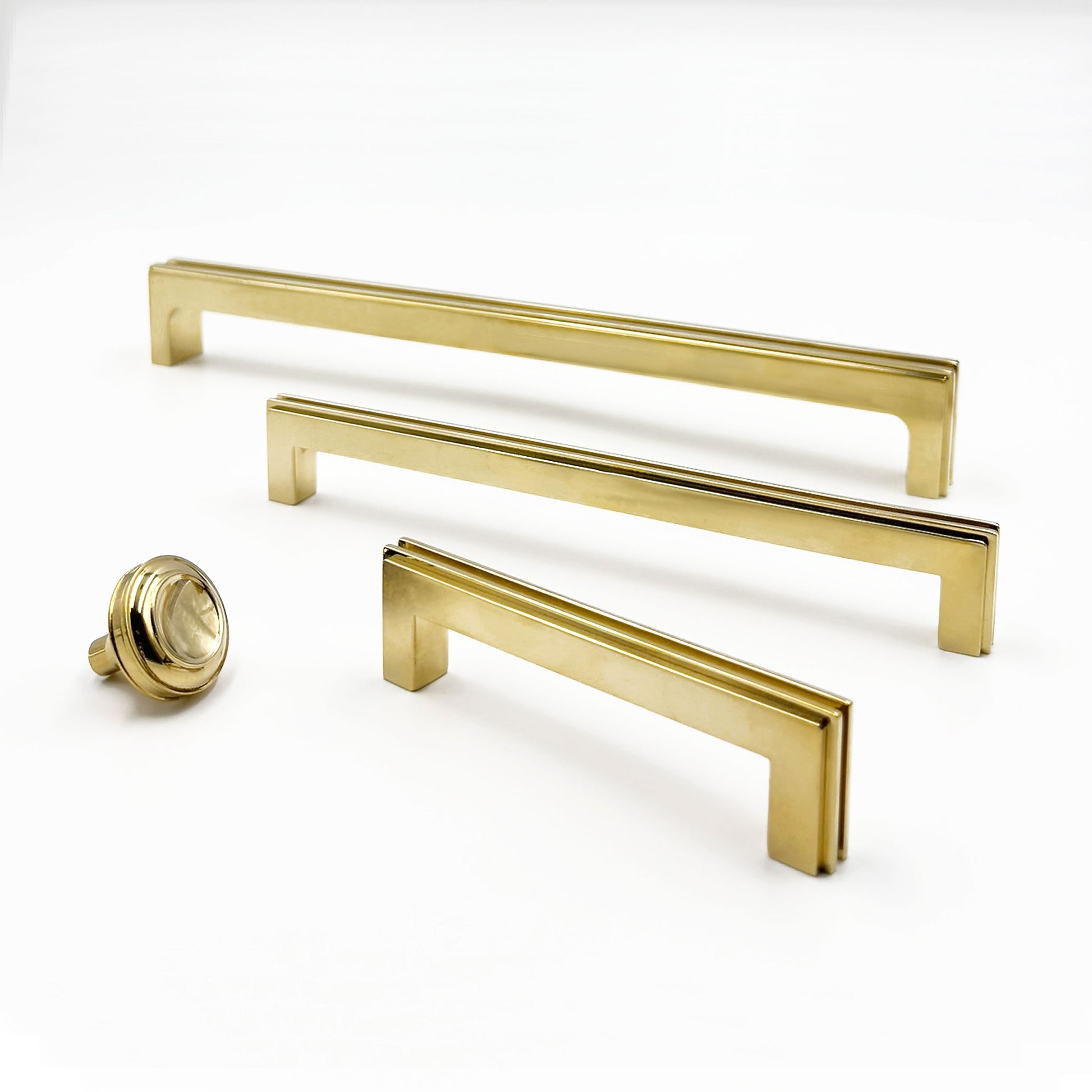 Grouping of three brass cabinet pulls and a knob on a white background