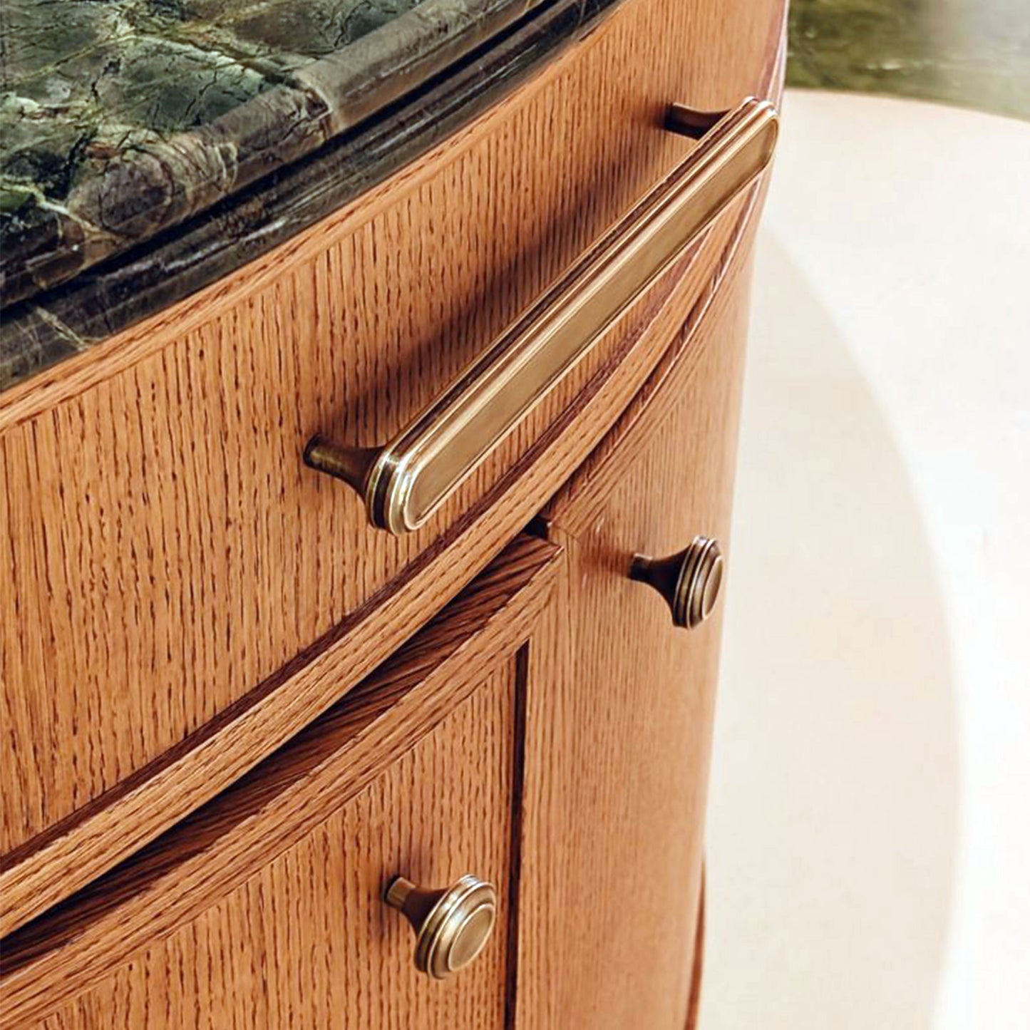 Close-up of wooden rounded front cabinets with burnished brass handles with a green marble top