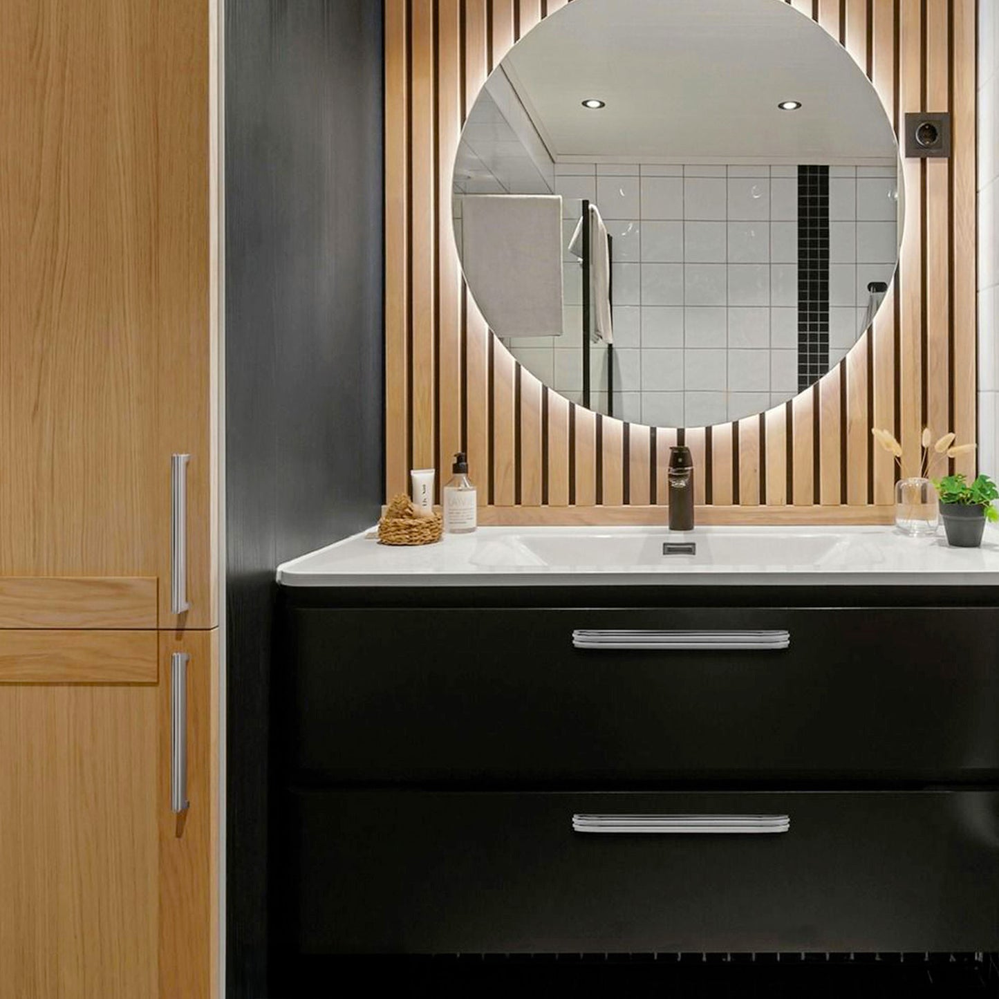 Bathroom vanity with round mirror, black cabinets, with Polished Chrome modern cup pulls and wooden accents.