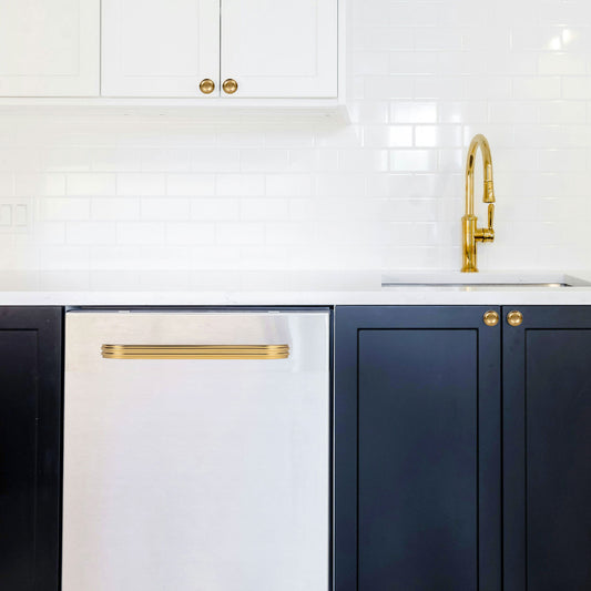 Modern kitchen with white and dark blue cabinetry, brass streamlined modern cup pulls, brass pulldown faucet and a white countertop.
