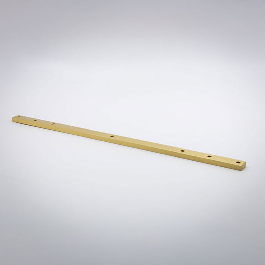 A long, thin satin brass metal bar with pre-drilled holes, photographed diagonally on a light gray gradient background.