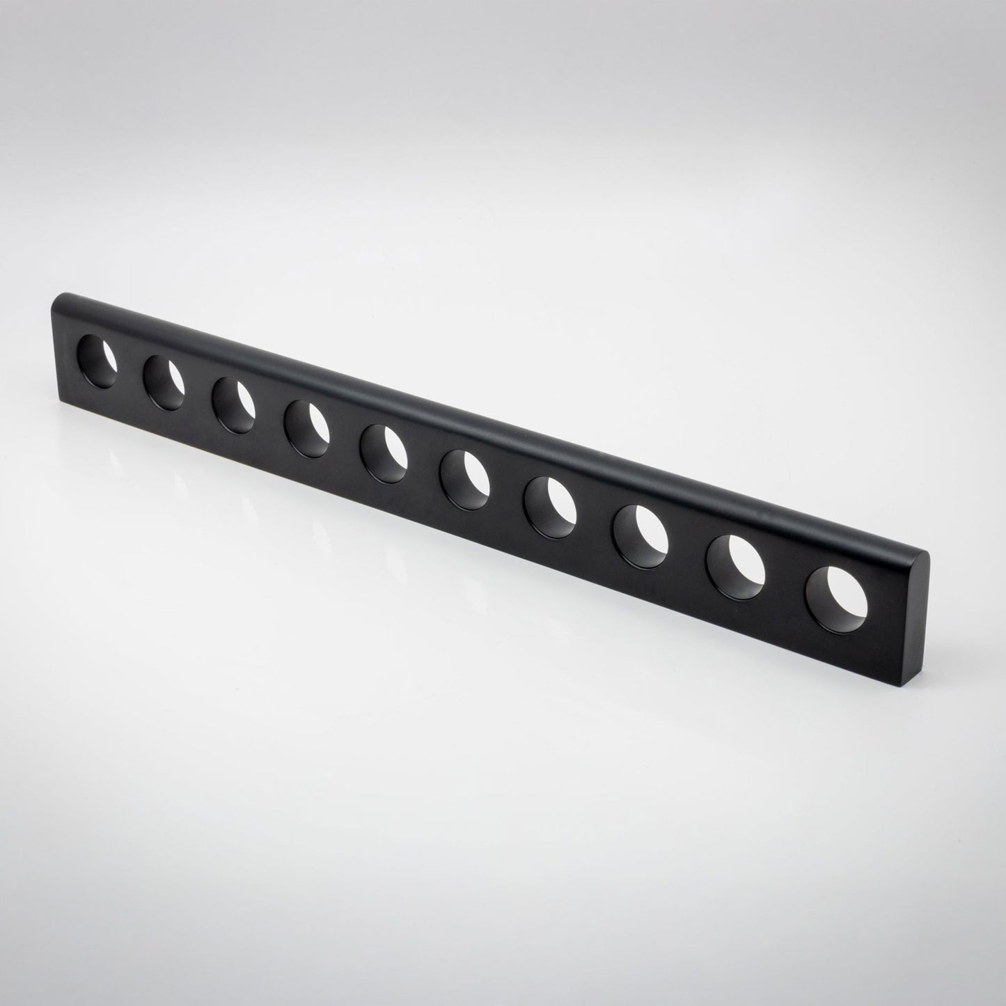 A long, black metal bar with ten evenly spaced circular holes, photographed diagonally on a clean white studio background.