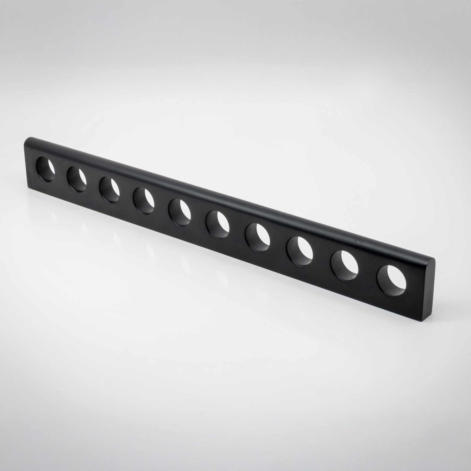 A long, black metal bar with ten evenly spaced circular holes, photographed diagonally on a clean white studio background.