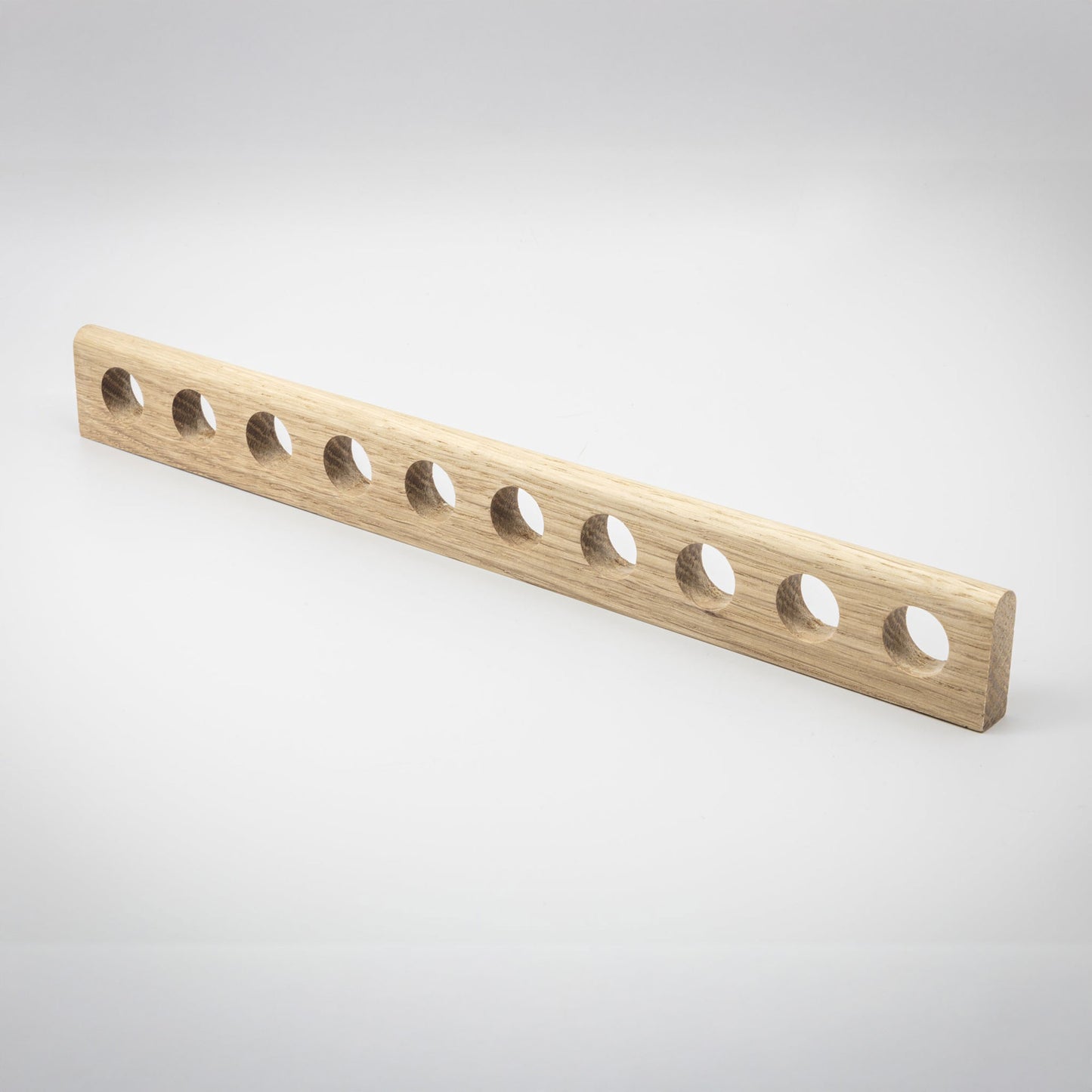 A light natural wood rectangular bar with ten evenly spaced circular holes, photographed on a clean light gray studio background.