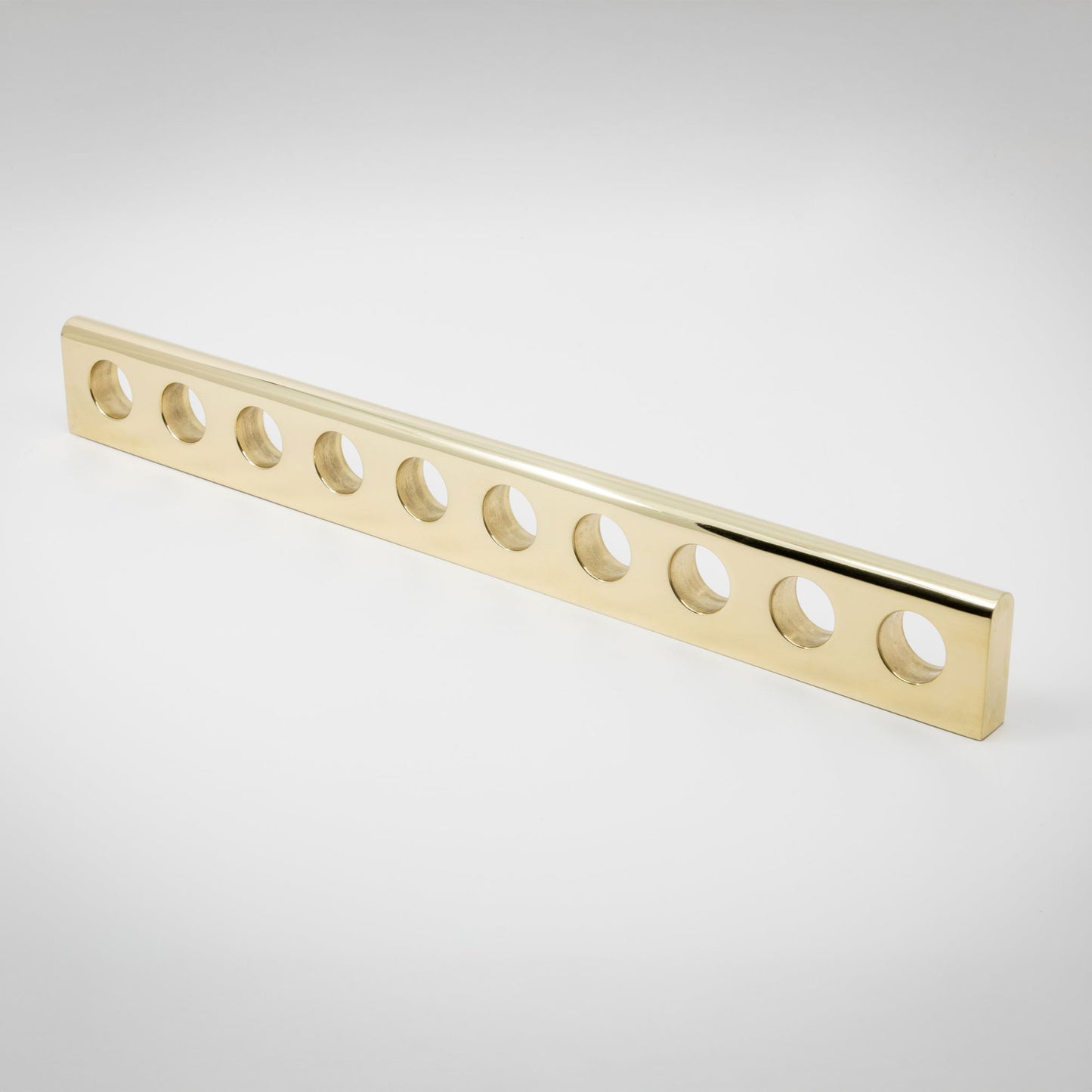 A long narrow light polished brass rectangular bar with ten evenly spaced circular holes, shown on a clean light gray studio background.