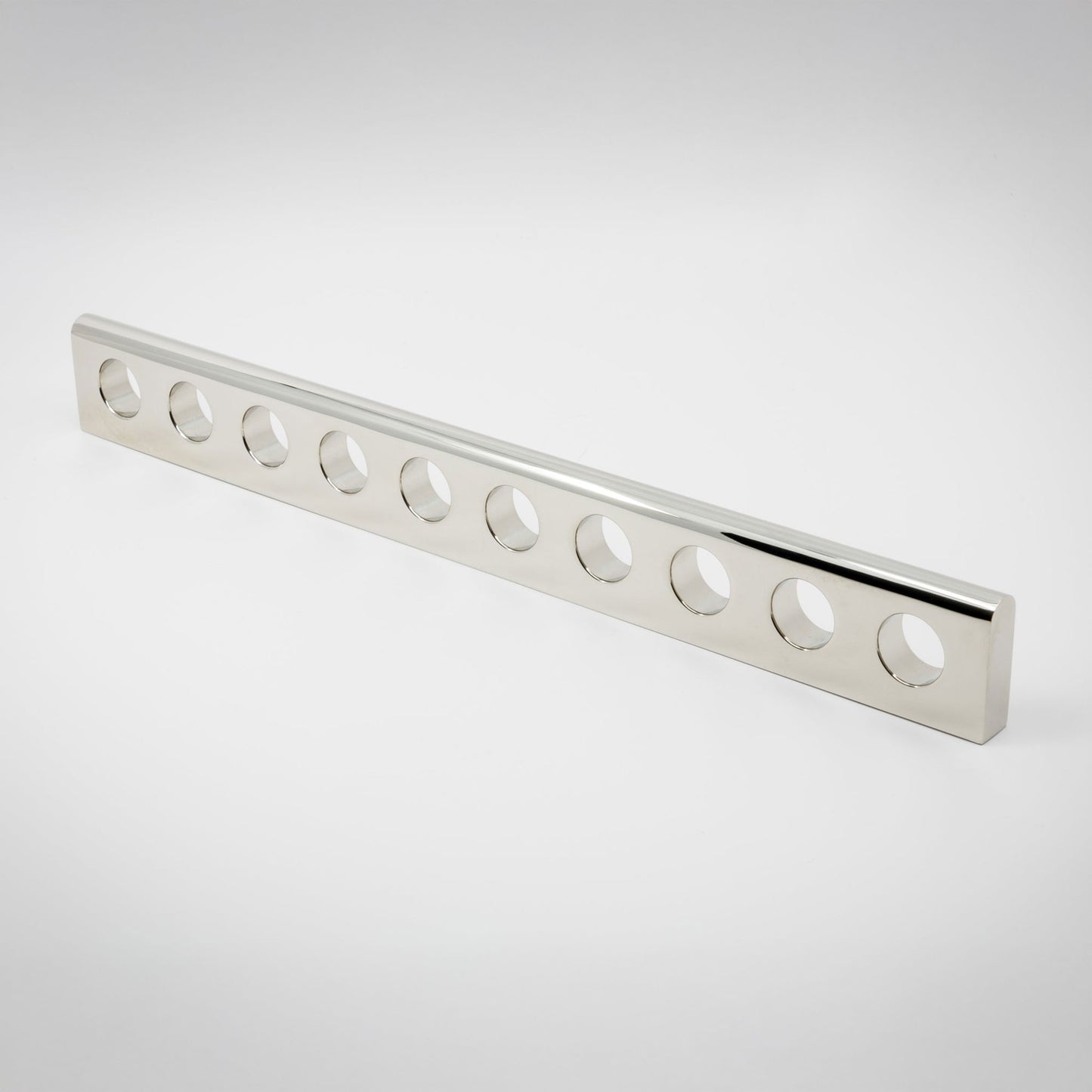 A long, narrow polished metal bar with a series of ten circular cutouts along one side, photographed on a clean light gray studio background.