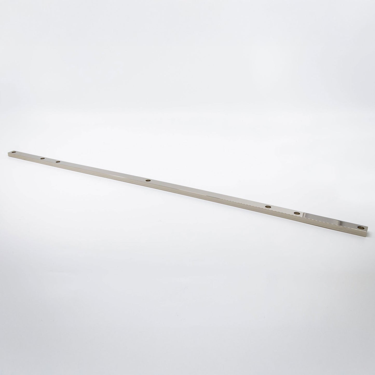 A long, slender metallic polished nickel with pre-drilled holes, photographed diagonally on a seamless white studio background.