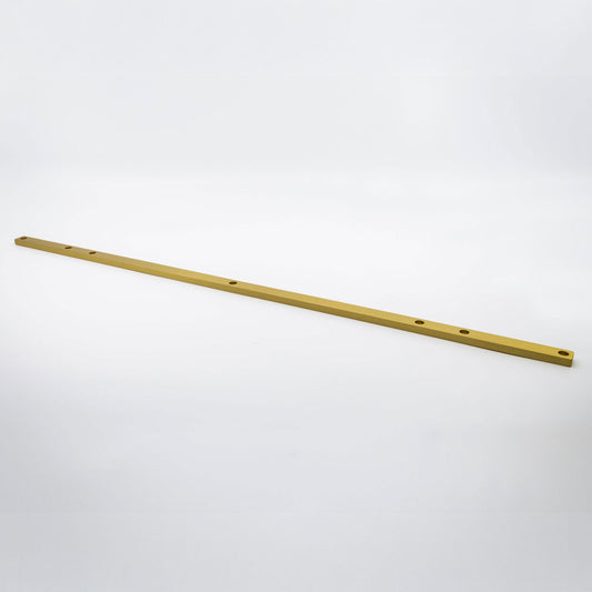 A long, thin metallic gold bar with pre-drilled holes, photographed diagonally on a seamless light gray background.