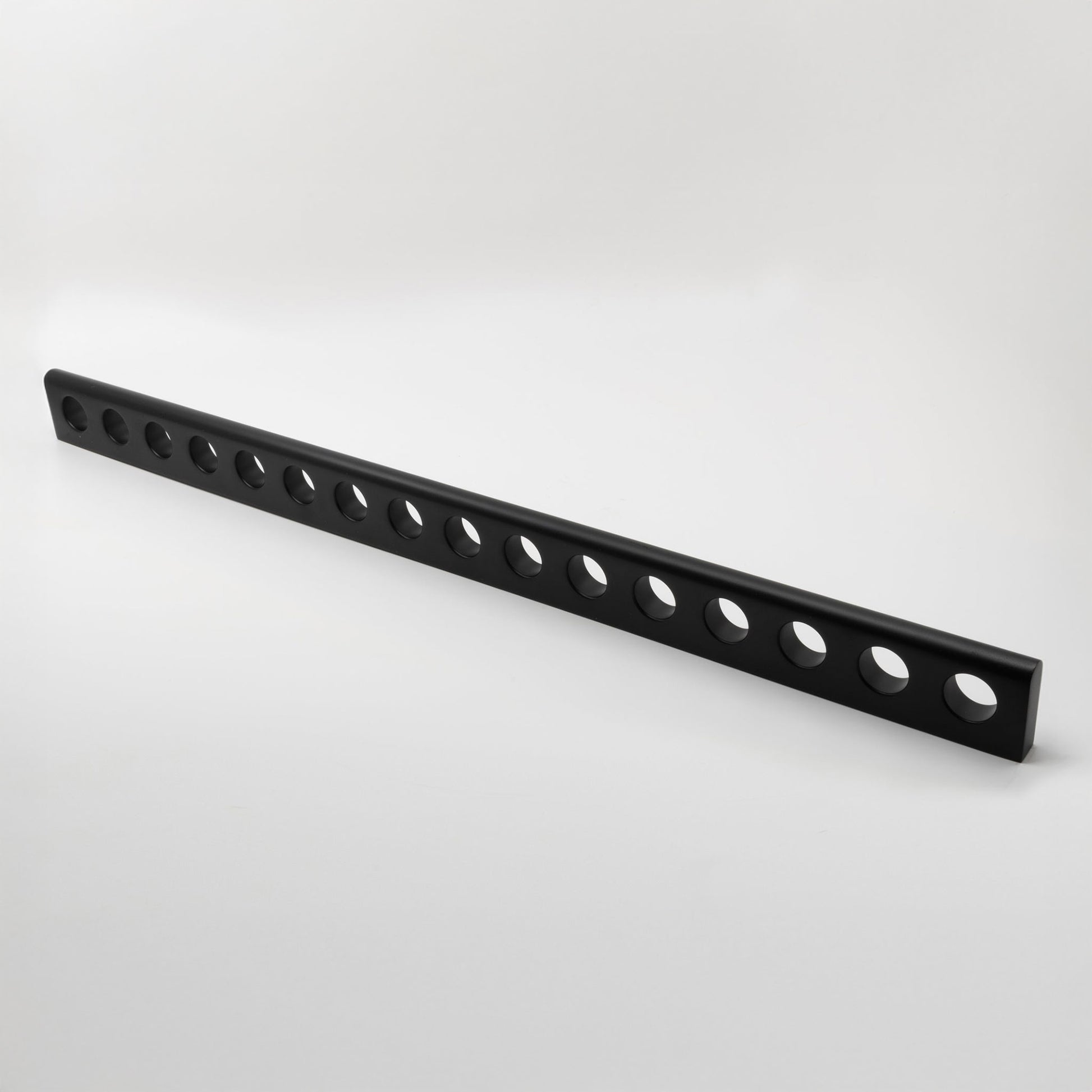 A long, black metal hardware handle with multiple circular cutouts, photographed diagonally on a clean white studio background.