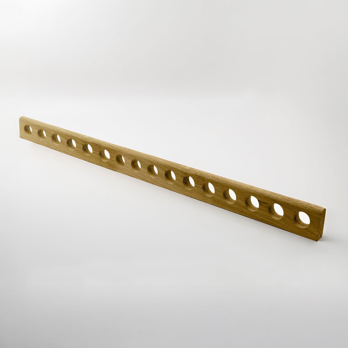 A long, narrow wooden handle with multiple evenly spaced circular holes, shown diagonally on a light gray studio background.