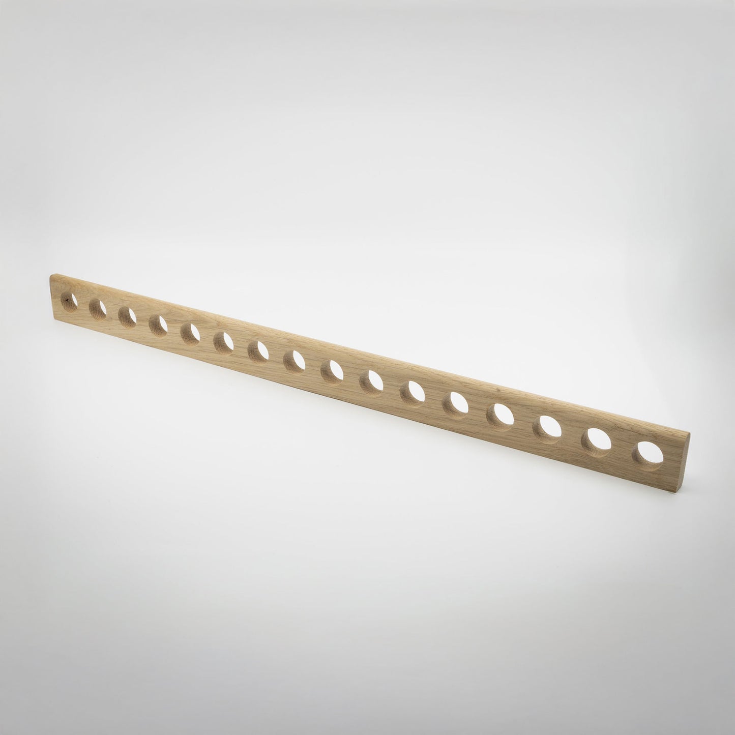 A light natural wood hardware handle with multiple evenly spaced circular cutouts, photographed diagonally on a clean white studio background.
