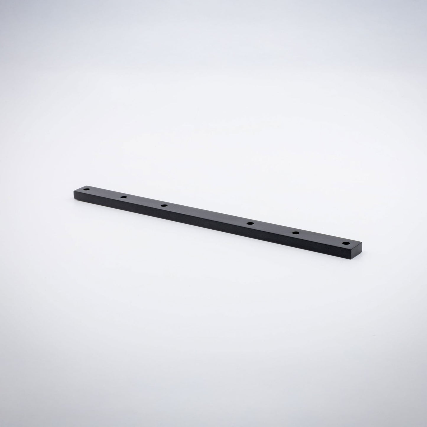 A long, narrow rectangular black brass base hardware bar with six evenly spaced circular holes, shown diagonally on a clean light gray studio background.