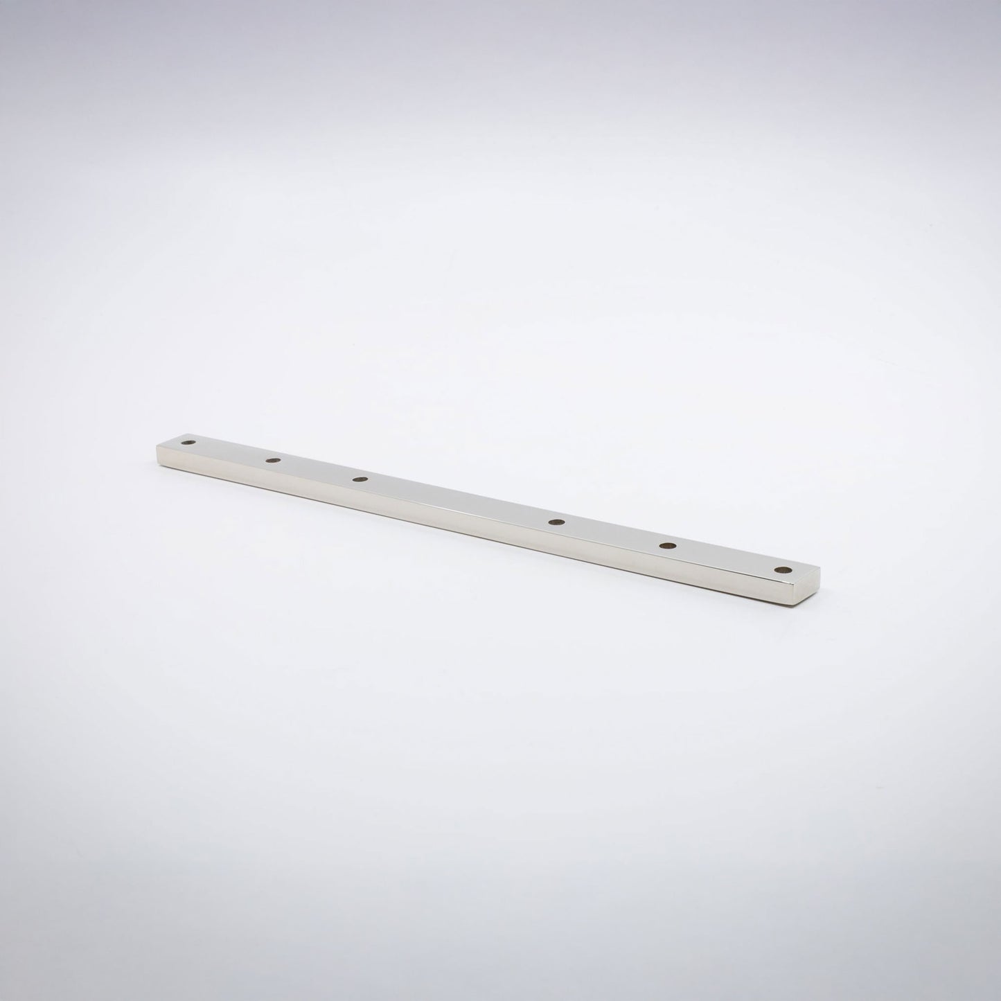 A long, narrow rectangular nickel base hardware bar with six evenly spaced circular holes, shown diagonally on a clean light gray studio background.