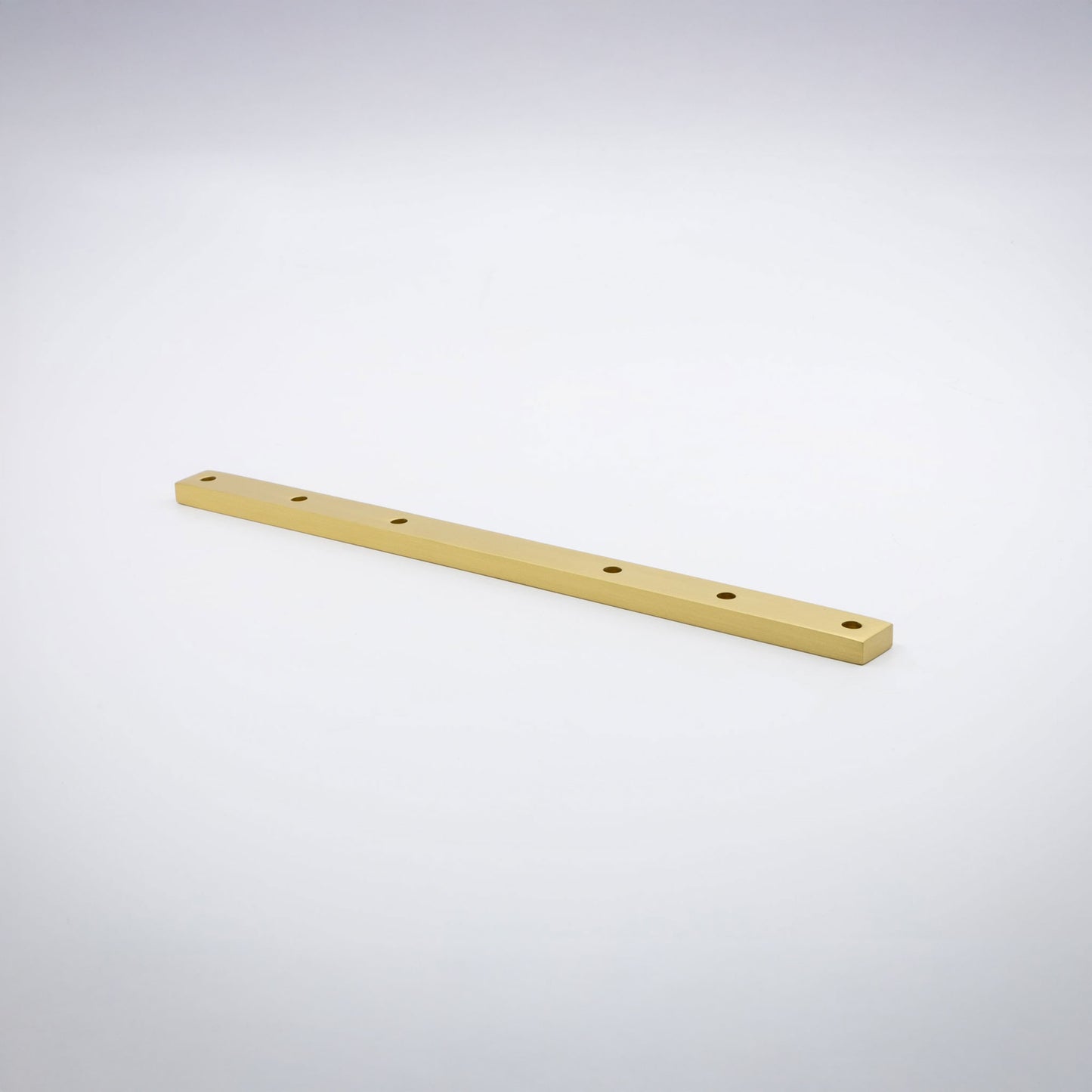 A long, narrow rectangular brass base hardware bar with six evenly spaced circular holes, shown diagonally on a clean light gray studio background.