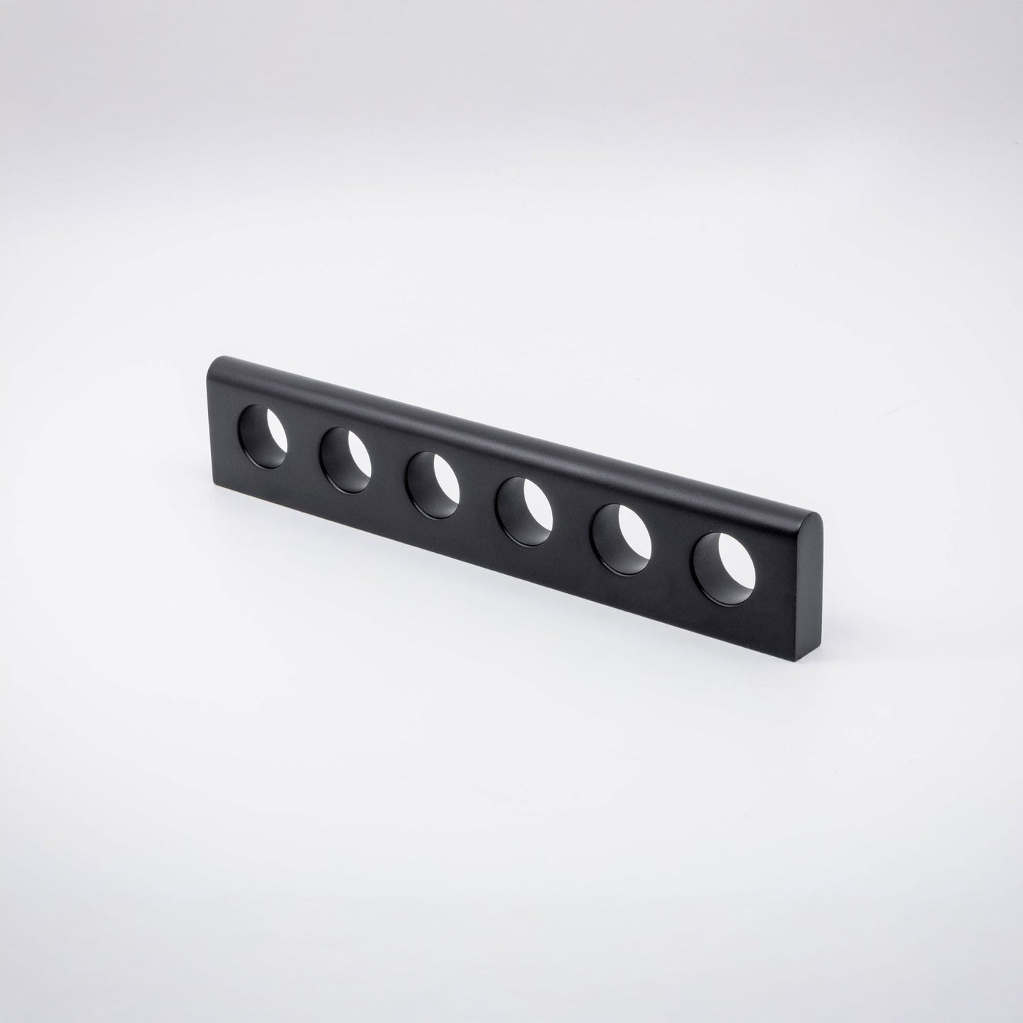 A black brass metal handle with six evenly spaced circular cutouts, shown on a clean white studio background.