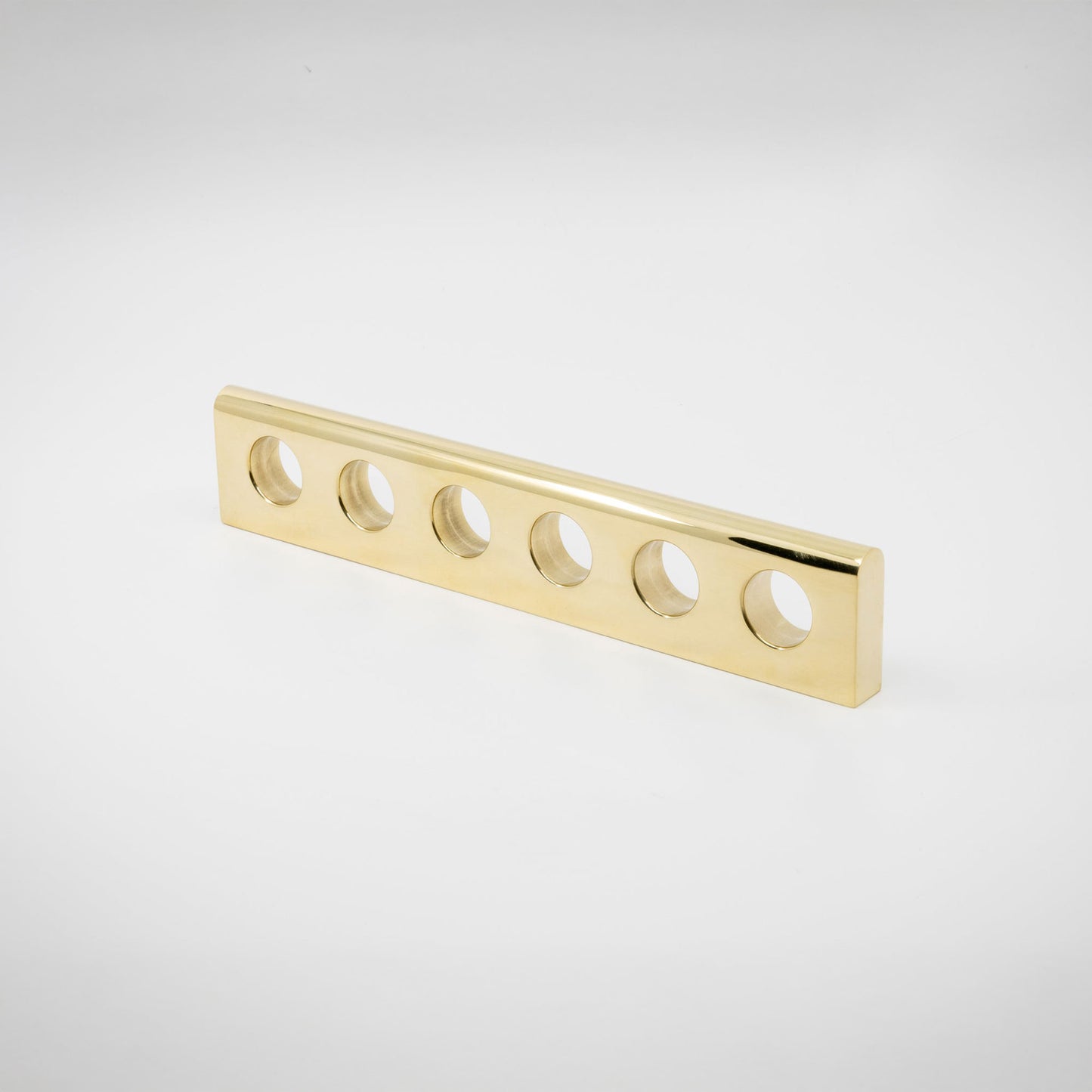 A gold-finished unlaquered brass metal hardware handle with six evenly spaced circular cutouts, shown on a clean white studio background.