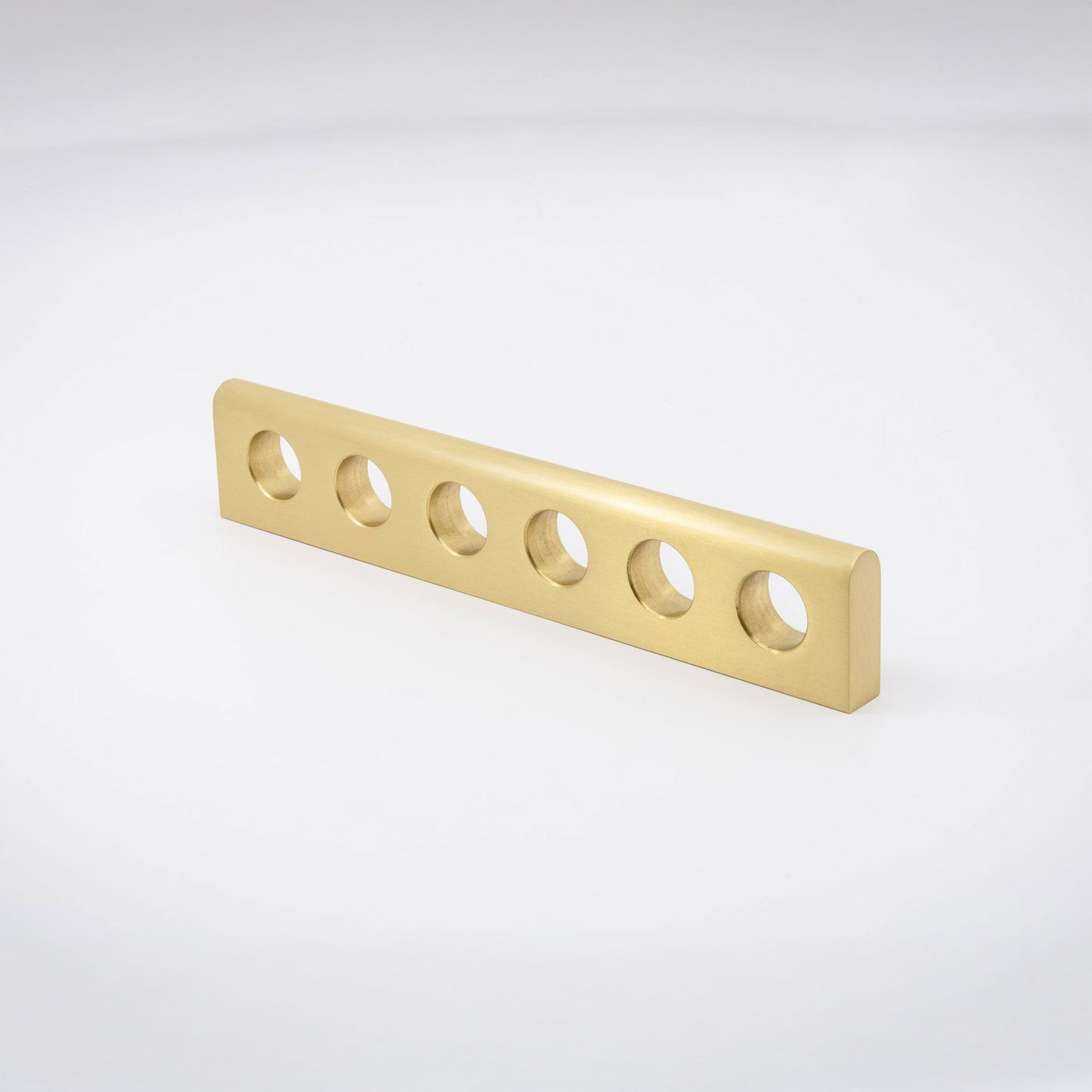 A gold-finished satin brass metal handle with six evenly spaced circular cutouts, shown on a clean white studio background.