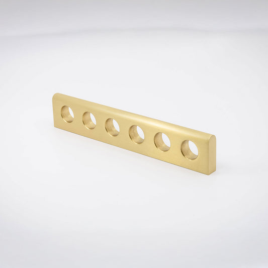 A gold-finished satin brass metal handle with six evenly spaced circular cutouts, shown on a clean white studio background.