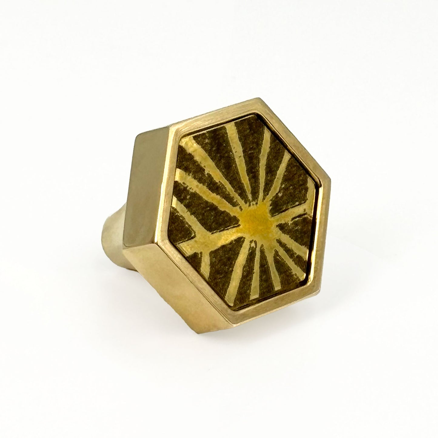 Hexagonal brass knob with etched sunburst design on a white background