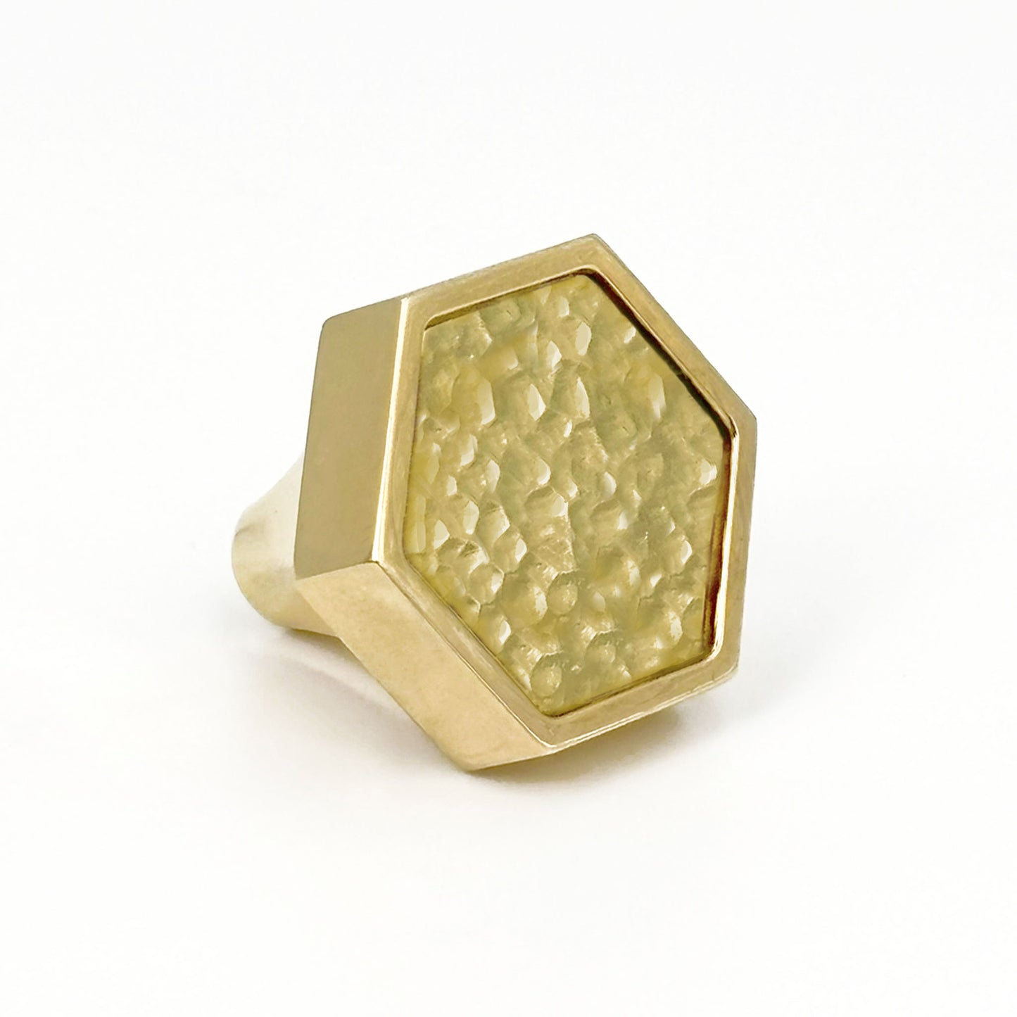 Brass Hex xhaped cabinet pull with surface texture on a white bacground