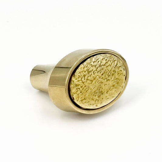 Brass oval cabinet knob with a textured surface on a white background