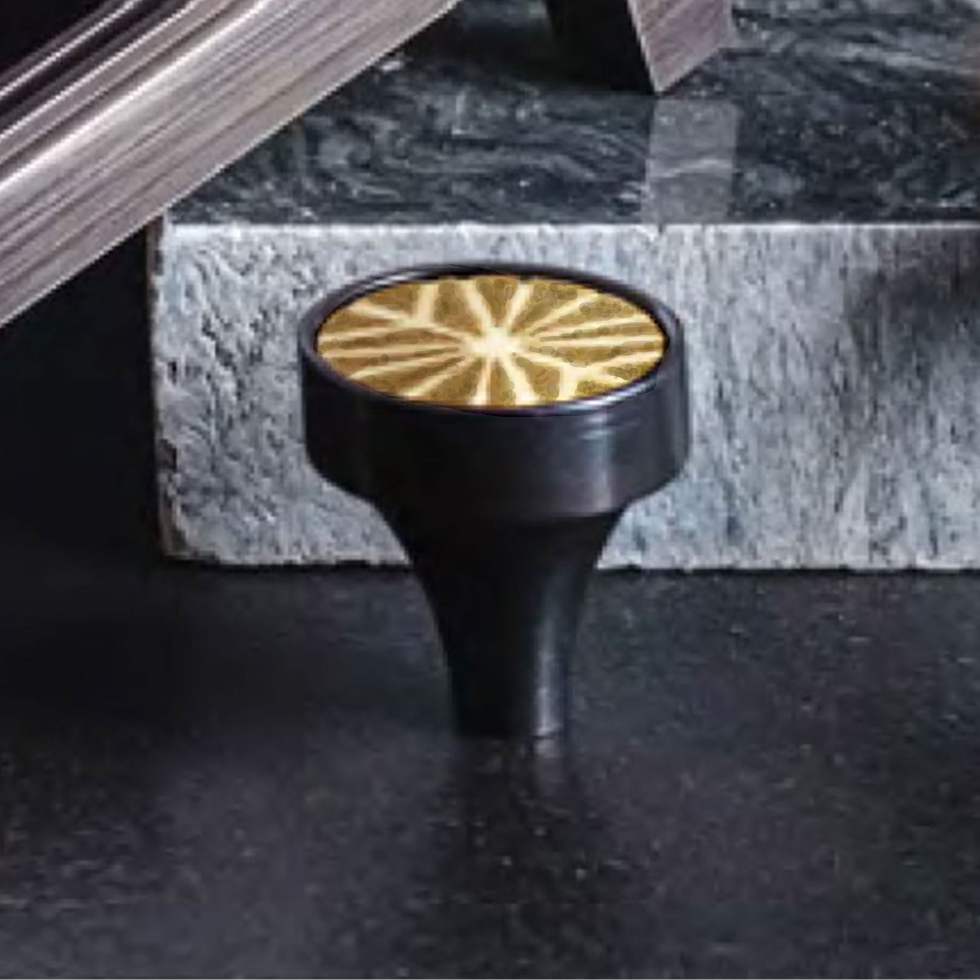 Patterned Aurora round cabinet pull in Black Lacquer finish on it side on a marble stone background
