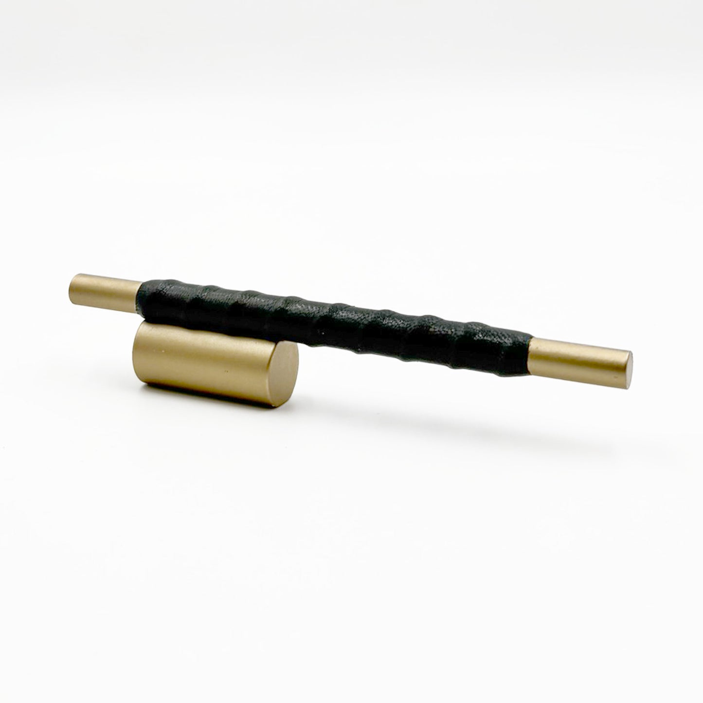 Satin Brass cylindrical cabinet pull with black leather wraped handle on a white background