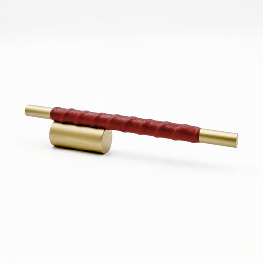 Satin Brass cylindrical cabinet pull with red leather wraped handle on a white background