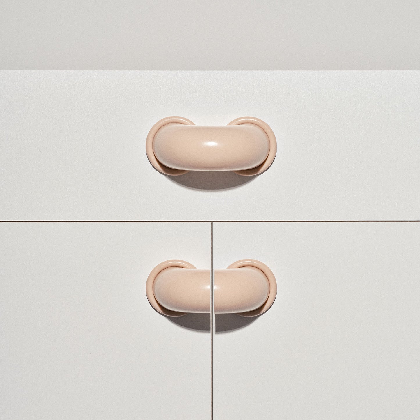 White cabinet with pale blush colored macaroni-shaped handles on a white background