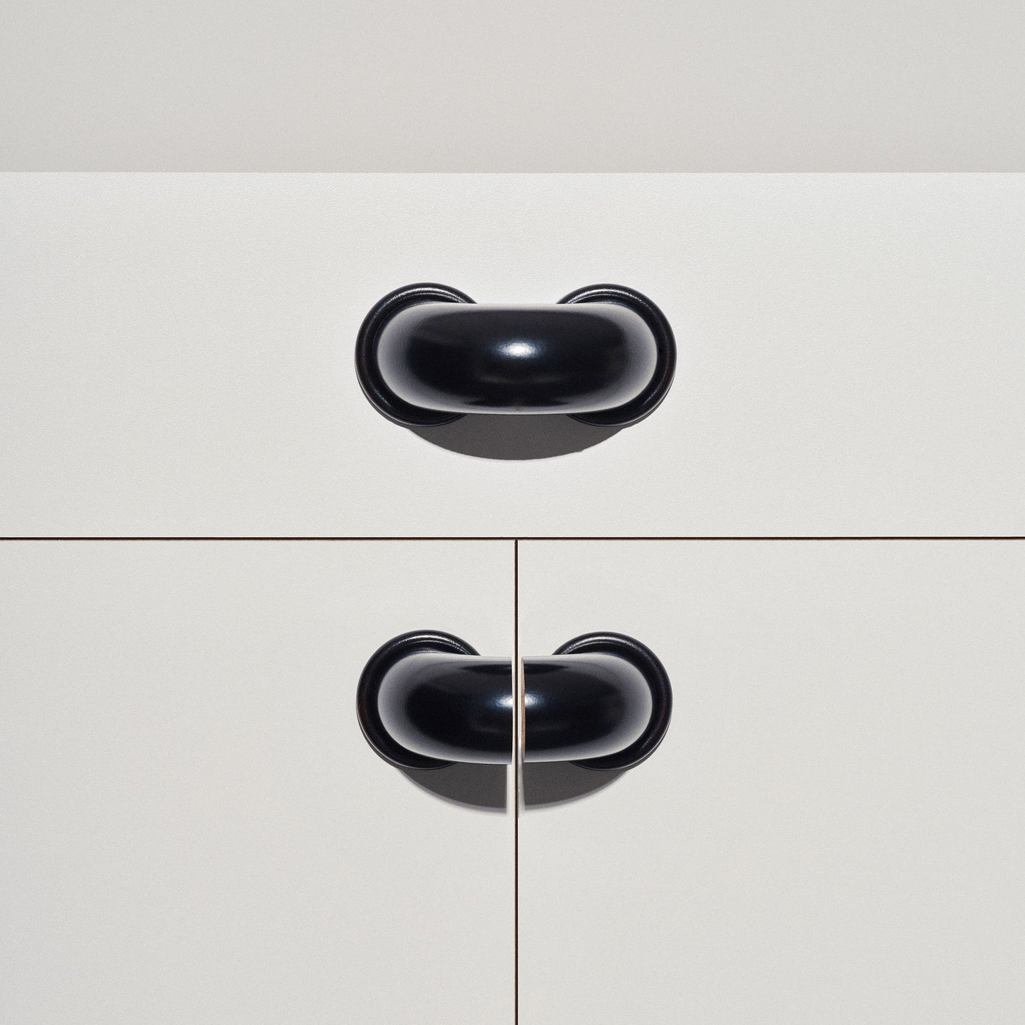 White cabinet with black colored macaroni-shaped handles on a white background