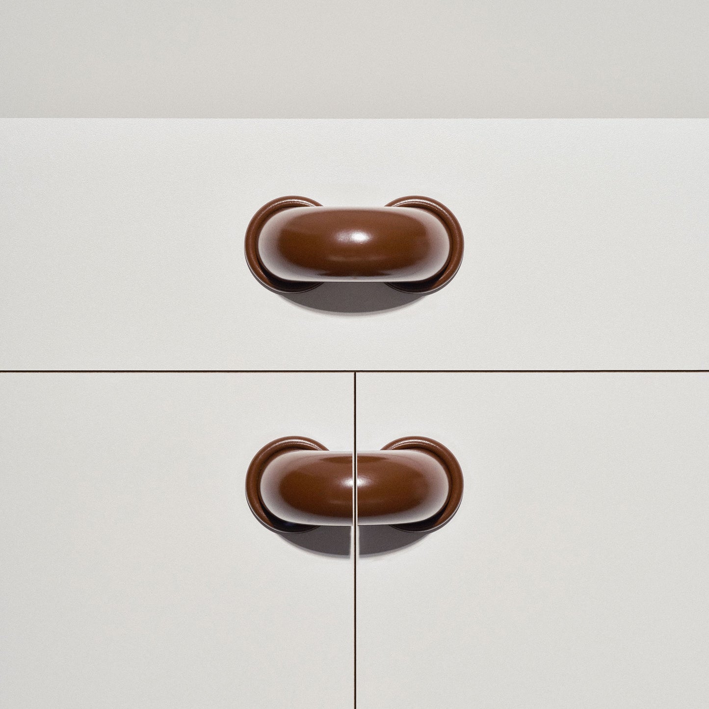 White cabinet with chocolate brown colored macaroni-shaped handles on a white background