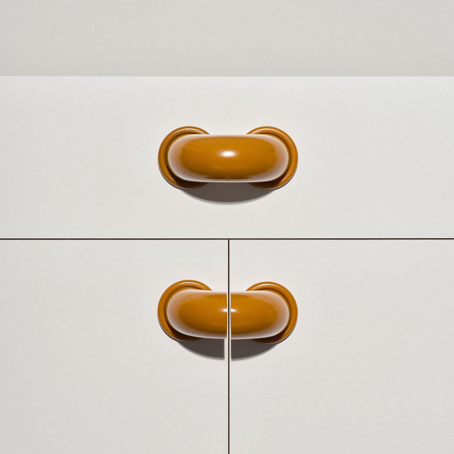 White cabinet with caramel colored macaroni-shaped handles on a white background