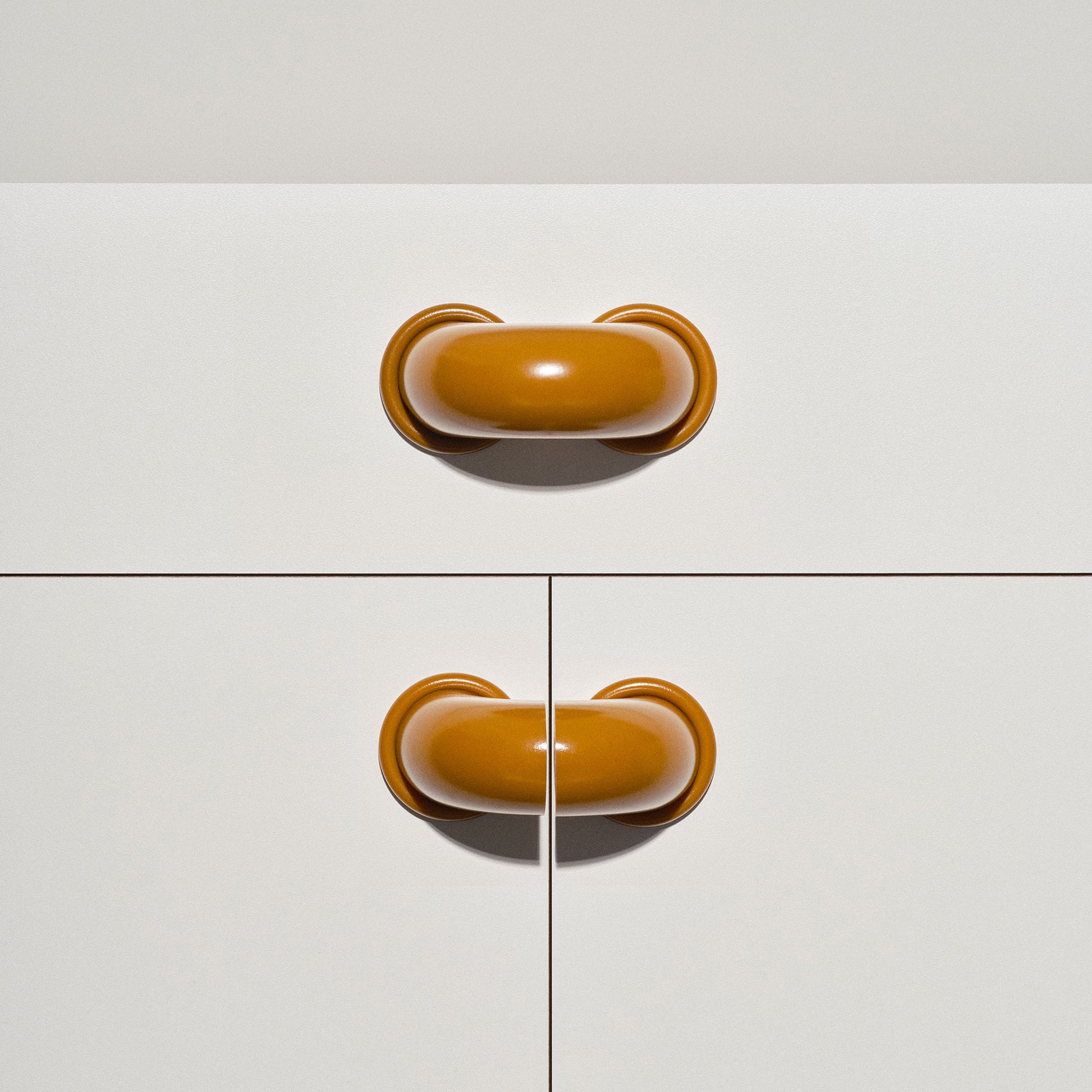 White cabinet with caramel colored macaroni-shaped handles on a white background