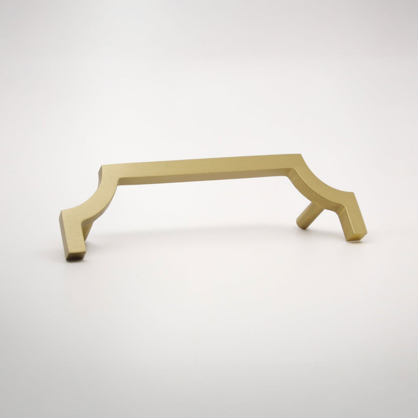 A satin brass-finished metal hardware pull with a decorative half quatrefoil-style frame and flat side pegs, shown on a light gray background.
