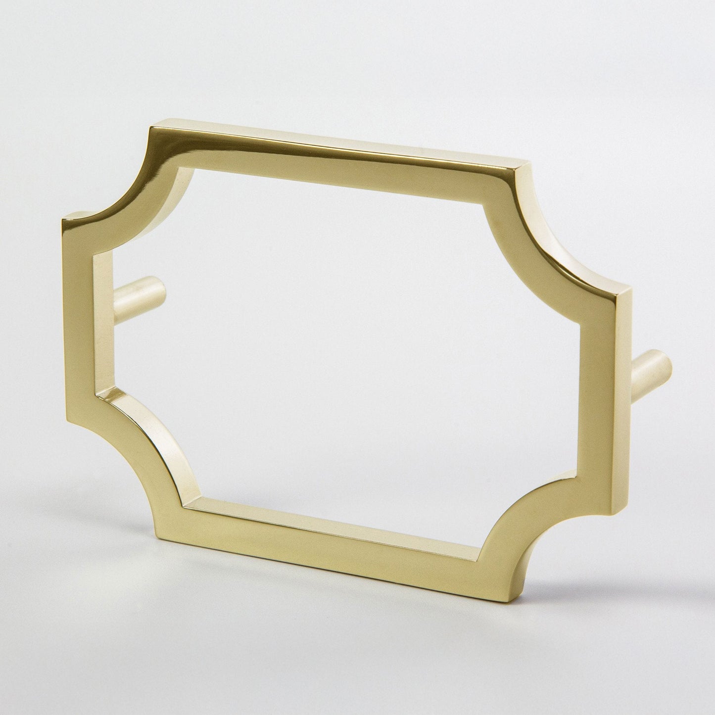 A gold-finished metal unlaquered brass hardware pull with a decorative quatrefoil-style frame and flat side pegs, shown on a light gray background.