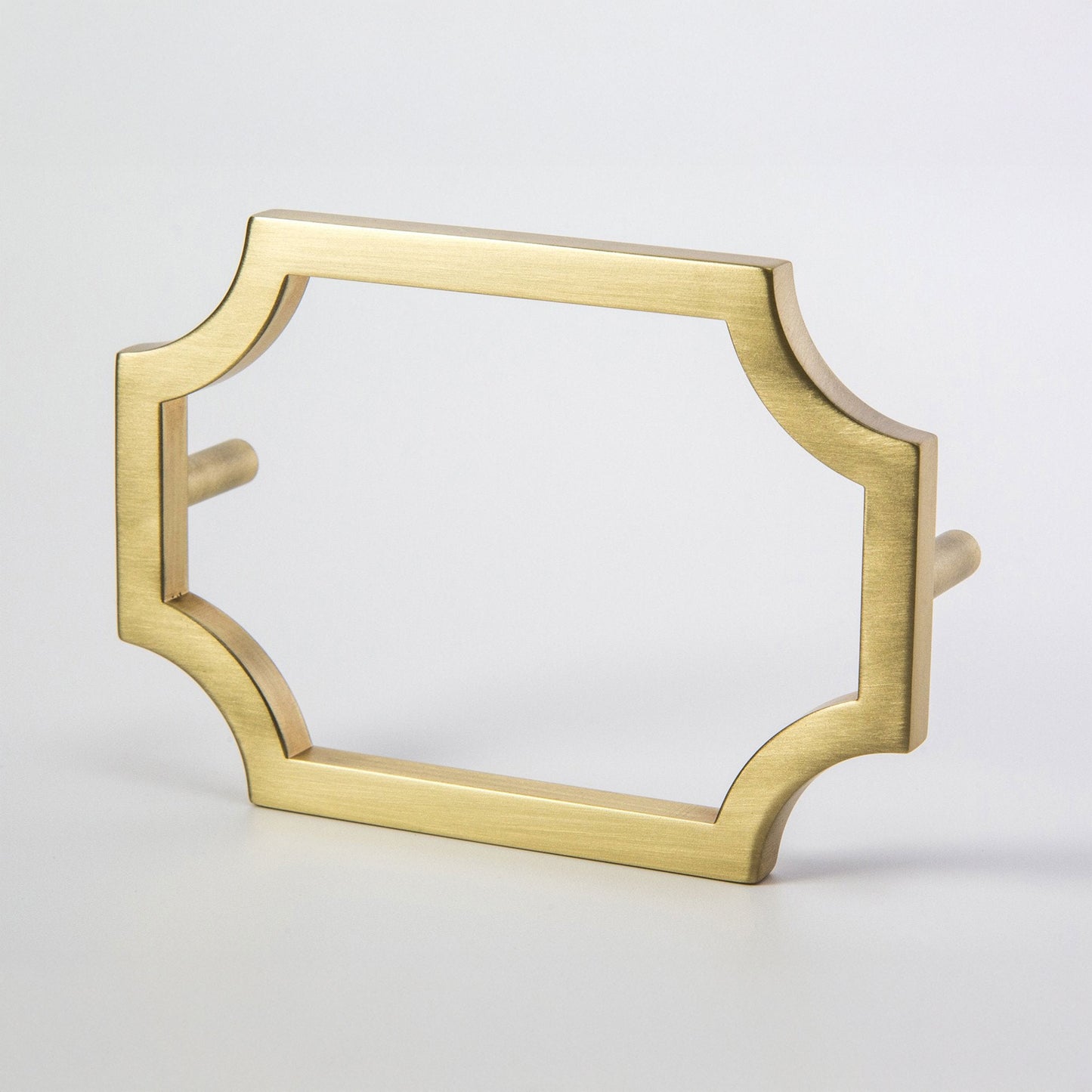 A gold-finished metal satin brass hardware pull with a decorative quatrefoil-style frame and flat side pegs, shown on a light gray background.