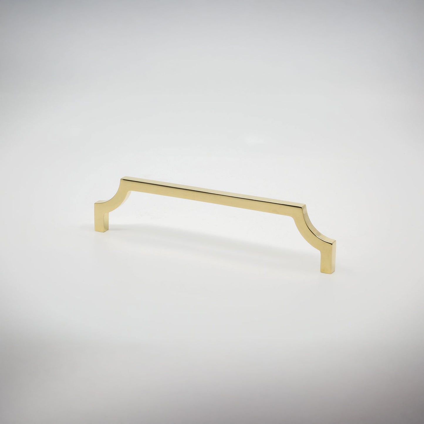 A single polished unlaquered brass cabinet pull handle with a curved, decorative top and bottom ends, shown on a clean light gray background.