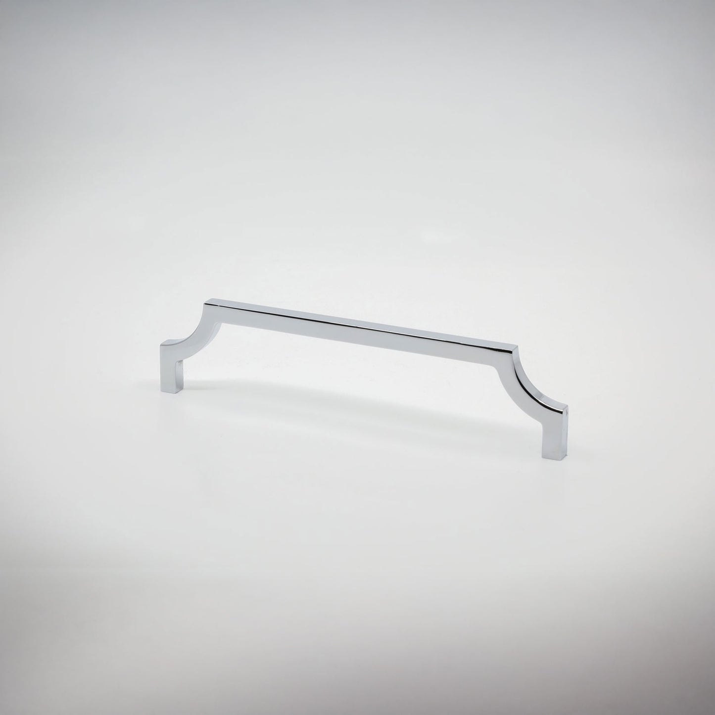 A single polished chrome cabinet pull handle with curved edges against a seamless light gray studio background.